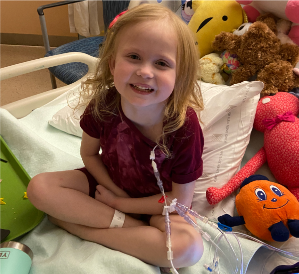 SickKids patient Tala sitting on her hospital bed with stuffed animals.