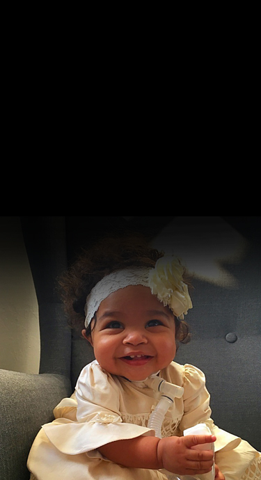 Noah smiling when she was a baby with a headband that features a flowe