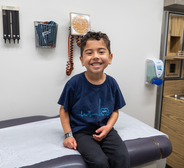 Caleb smiling, sitting on an exam table at SickKids.