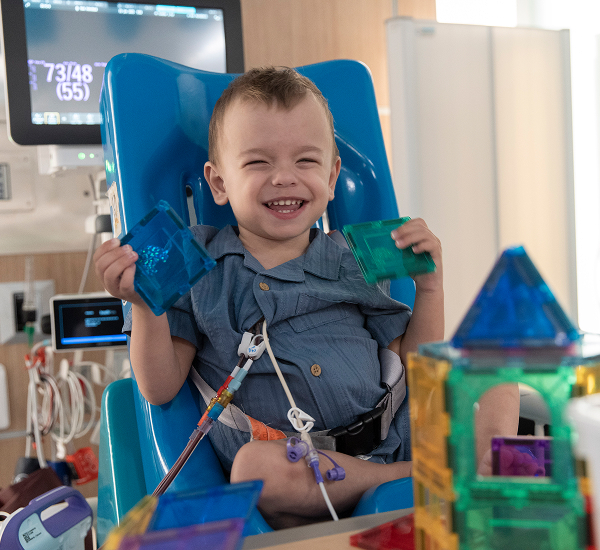 Noah smiling, in a hospital room at SickKids playing with blocks. 