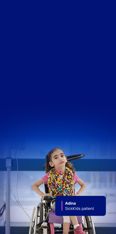 Adina at SickKids, sitting in her wheelchair and smiling, wearing colorful bravery beads necklaces.