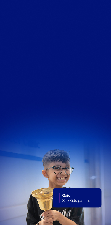 Qais at SickKids, smiling and holding a golden bell.