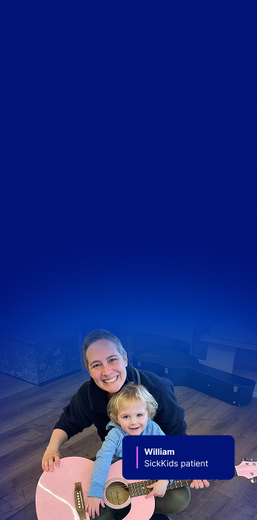William at home, smiling while holding a pink guitar with a caregiver behind him.