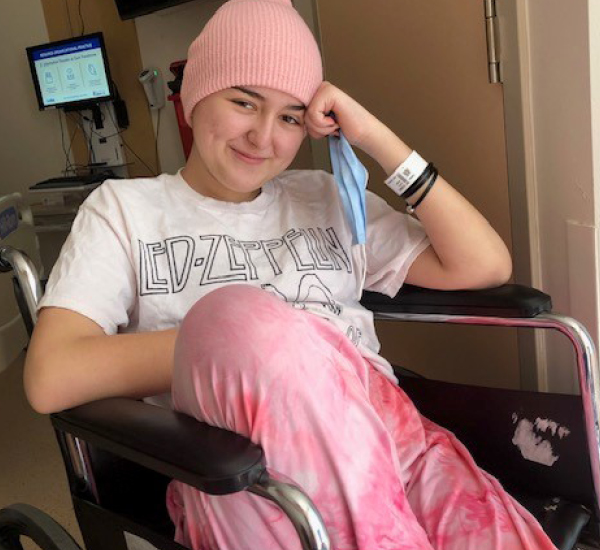Juliet sitting in a wheelchair at SickKids, smiling and wearing a pink hat.