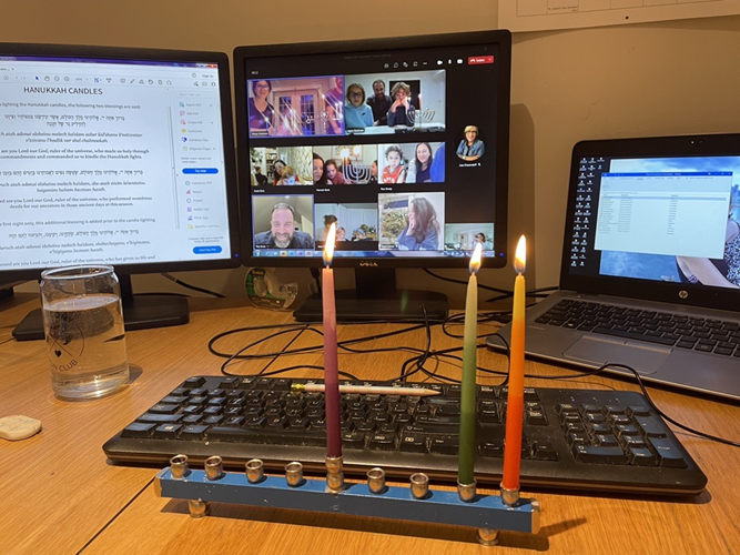 A virtual Chanukah gathering with individuals from the Shalom SKF employee resource group shown on a computer screen along with three lit candles in front of a keyboard.