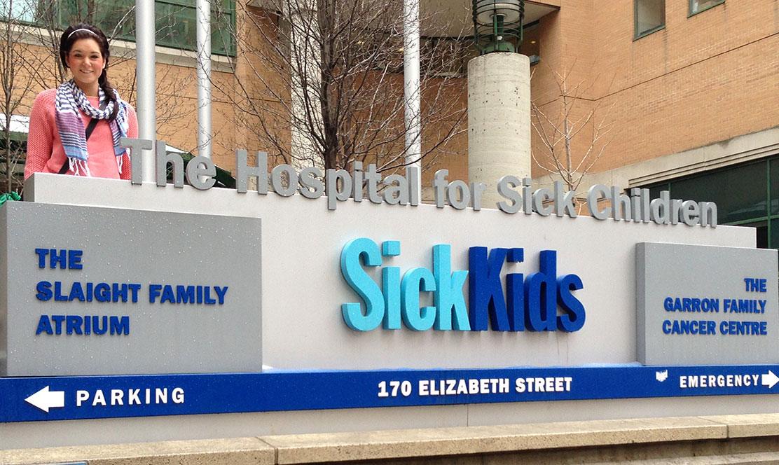 Former SickKids patient stands beside hospital sign