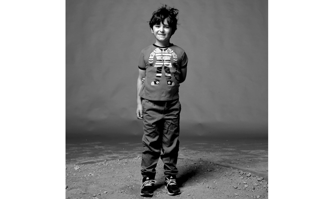 Young boy standing with one arm behind back and smiling