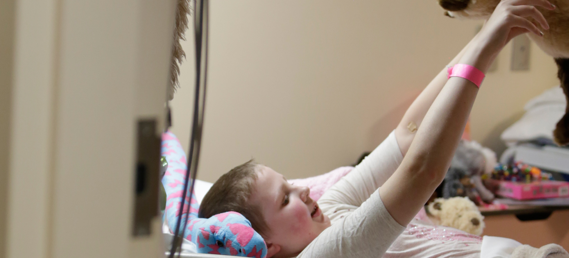 Girl lying in hospital bed holding up teddybear