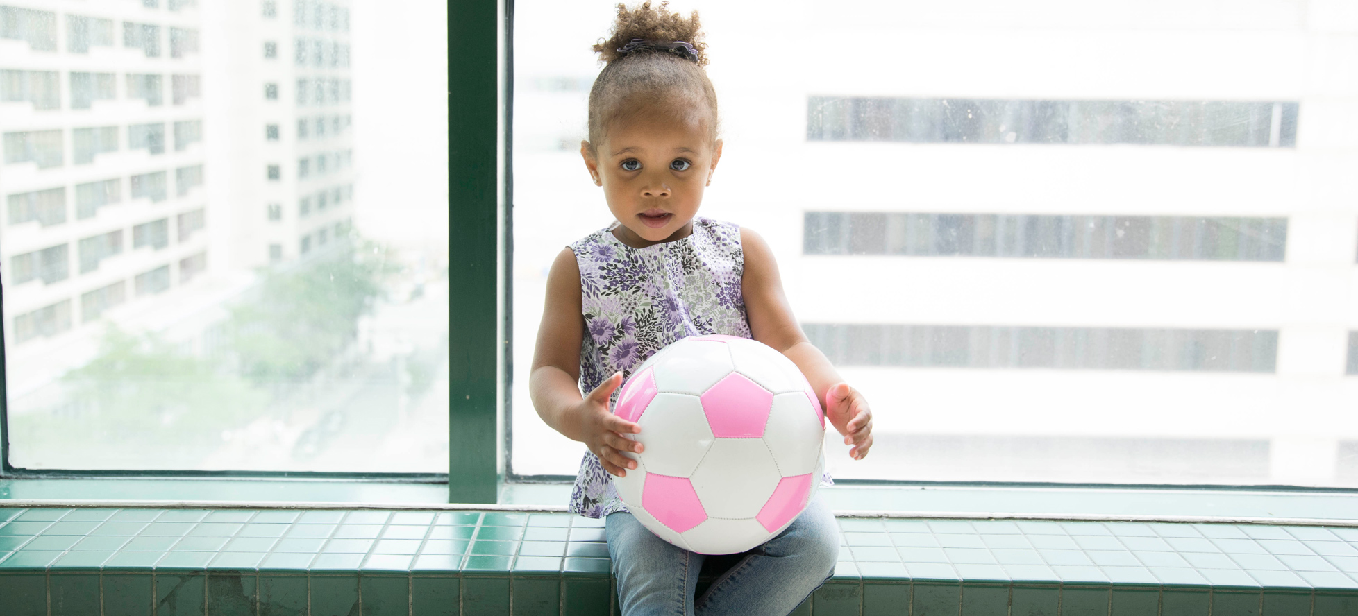 Girl sitting by window with pink soccer ball