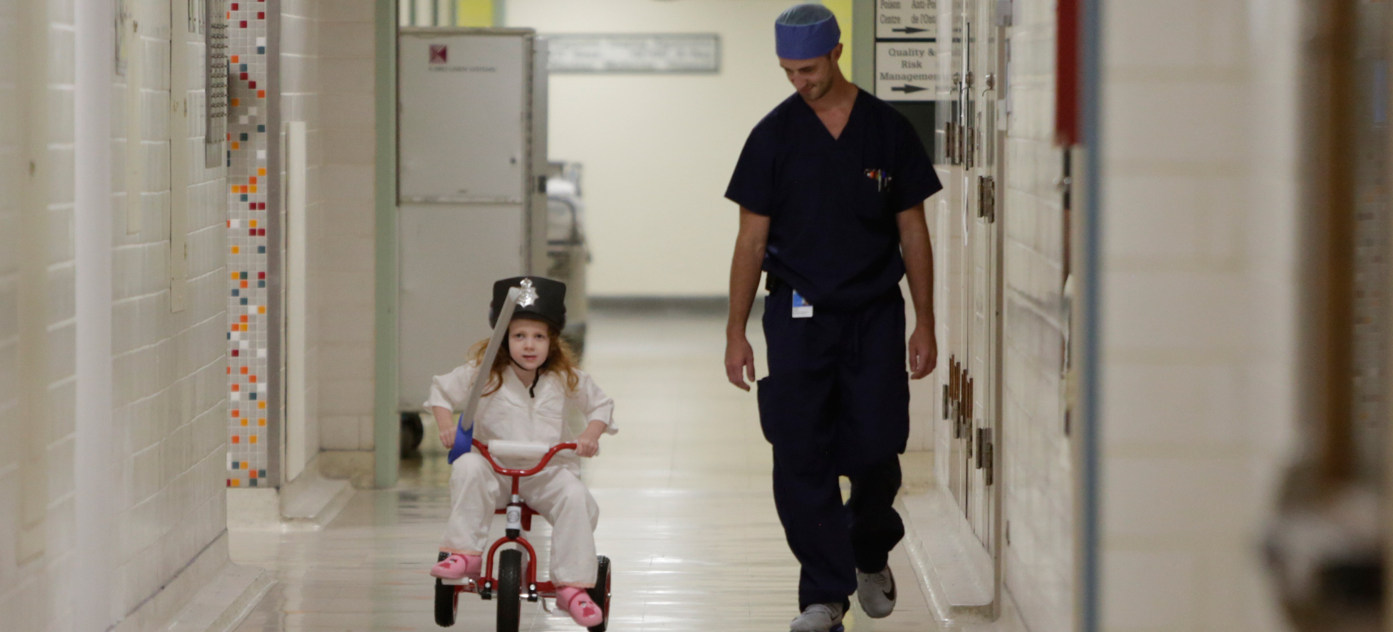 girl riding tricycle down hospital hallway