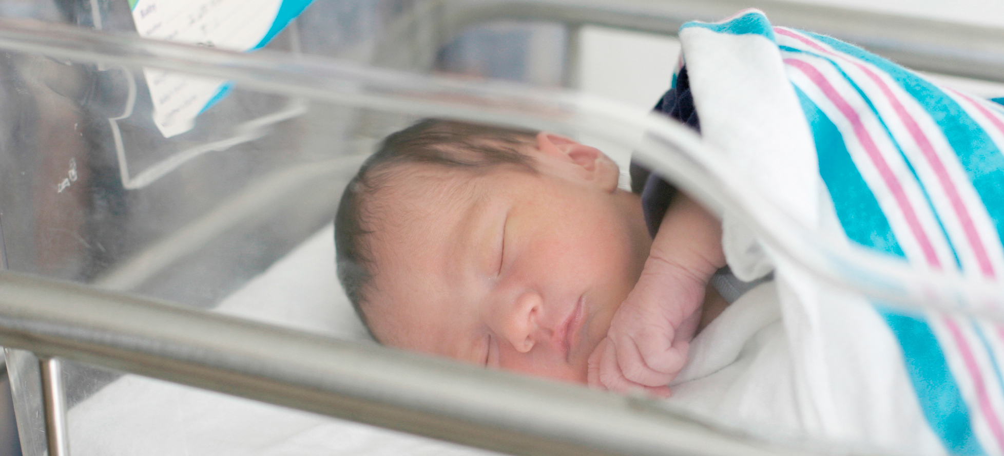Little baby in blanket lying in clear crib
