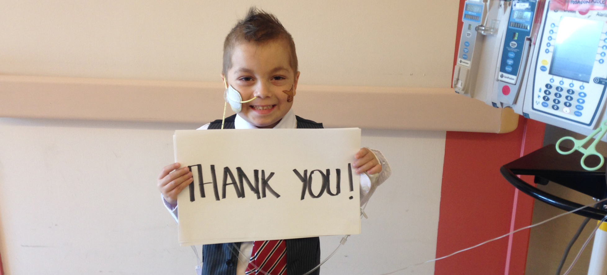 Little boy with IV pole holding up thank you sign