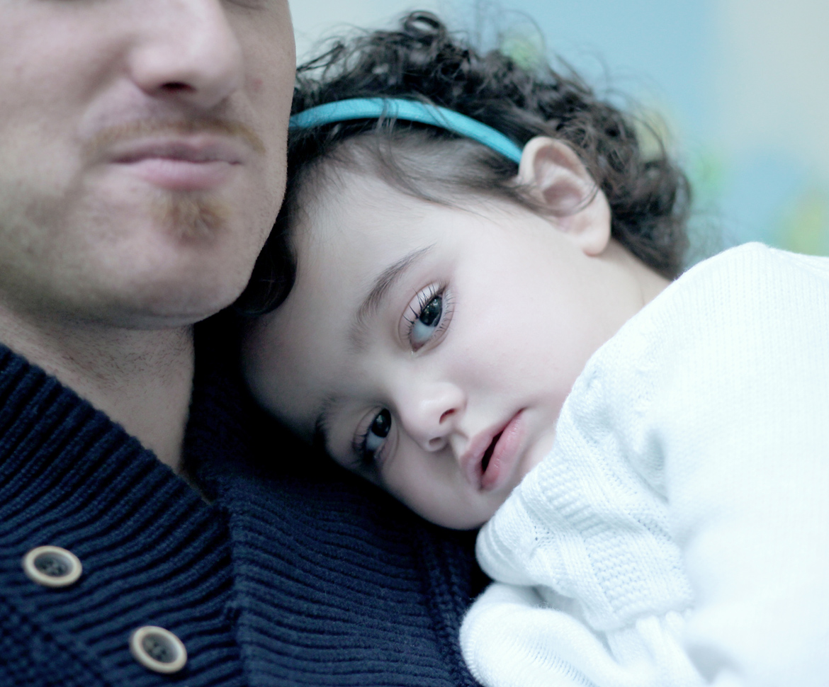 Little girl with headband and curly hair resting head on dad's shoulder