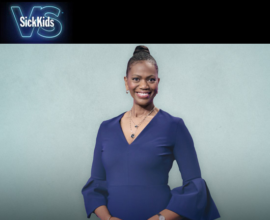 The Sickkids Foundation new CEO Jennifer Bernard. She is wearing a navy blue dress with long sleeves that flare at the cuff. She is wearing two necklaces with pendants and hoop earrings. She is smiling. She has brown skin and brown hair that is being worn in a bun.